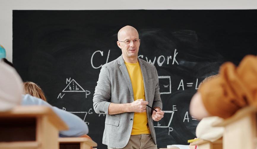 Moški stoji v učilnici pred šolsko tablo.